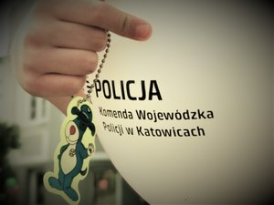 Ręka dziecka trzymająca dmuchany balon z napisem Komenda Wojewódzka Policji w Katowicach.