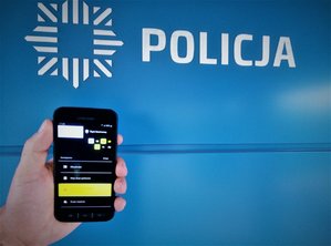 Dłoń trzymająca telefon, na tle logo z napisem Policja