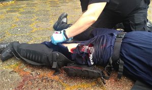 Policjant podczas ćwiczeń symulacyjnych opatruje zranioną nogę innego policjanta.