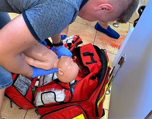 Mężczyzna podczas ćwiczeń z pierwszej pomocy wykonuje czynności ratunkowe z użyciem fantomu - niemowlaka.