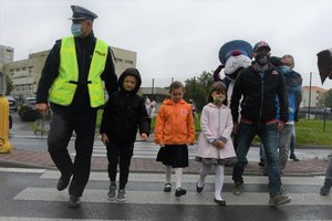 Zdjęcie kolorowe. Policjanci i Adam Małysz przeprowadzają dzieci przez ulicę