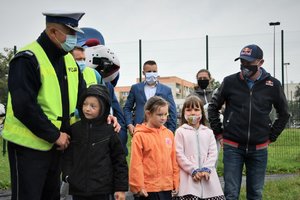 Zdjęcie kolorowe. Policjanci i Adam Małysz przeprowadzają dzieci przez ulicę