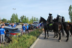 Na zdjęciu widoczna grupa osób na parkingu, obok czterech policjantów na koniach. Policjanci wyposażeni są w kaski i kamizelki.