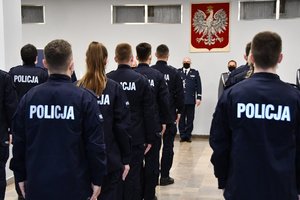 Policjanci stojący tyłem, w tle Komendant Wojewódzki Policji w Katowicach podczas przemówienia.