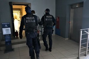 umundurowani policjanci prowadzą zatrzymanego korytarzem komendy