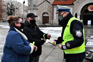 Policjant rozmawia z ludźmi, którym wręczył odblaskowe bransoletki.