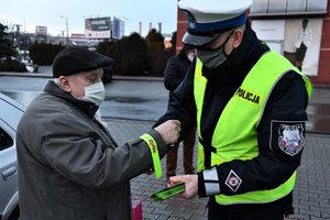 Policjant zakłada na rękaw kurtki starszego mężczyzny odblaskową bransoletkę.