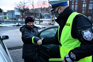 Policjant zakłada kobiecie na rękaw kurtki odblaskową bransoletkę.