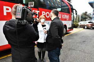 Pracownica Mobilnego Punktu Poboru Krwi udziela wywiadu telewizji. W tle autobus, w którym oddawana jest krew.