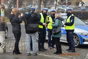 Na zdjęciu policjanci oraz członkowie kabaretu przebrani w policyjne mundury. Jeden z kabareciarzy trzyma w dłoni tulipana, obok dwie osoby robiące zdjęcia. W tle policyjny radiowóz.