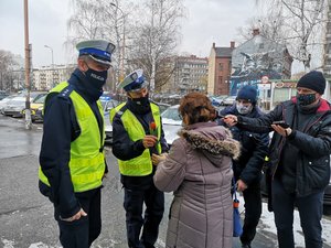 Na zdjęciu policjant oraz członek kabaretu przebrany w policyjny mundur, trzymający w dłoni tulipana, którego wręcza kobiecie. Obok stoją przedstawiciele mediów, jeden z mężczyzn trzyma mikrofon.
