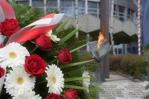 Zdjęcie kolorowe. Widoczny fragment Grobu Policjanta Polskiego, zapalony znicz oraz część wieńca kwiatów