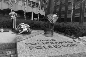Zdjęcie czarno-białe. Widoczny fragment Grobu Policjanta Polskiego, zapalony znicz oraz część wieńca kwiatów