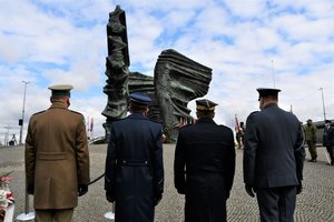 Przedstawiciele służb mundurowych stoją tyłem naprzeciw pomnika Powstańców Śląskich.