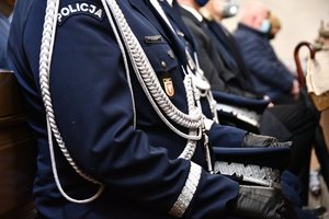 Policjanci siedzą w kościelnej ławce. Zbliżenie na czapkę generalską i policyjny mundur.