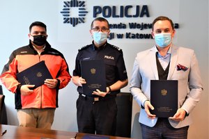 Na zdjęciu Komendant Wojewódzki Policji oraz Dyrektorzy chwilę po podpisaniu porozumień. Stoją przy biurku i trzymają w dłoniach porozumienia, które znajdują się w teczkach z napisem Komendant Wojewódzki Policji w Katowicach.