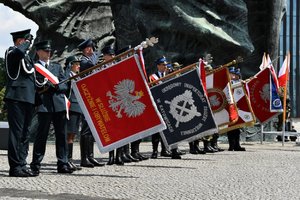 Poczty sztandarowe służb mundurowych stojące przy pomniku podczas śpiewania Hymnu Rzeczypospolitej Polskiej.