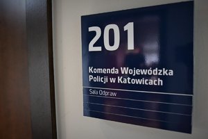 Tabliczka przed drzwiami z numerem 201 i napisem Komenda Wojewódzka Policji w Katowicach Sala Odpraw.