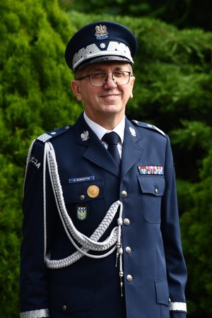 Komendant Wojewódzki Policji w Katowicach stoi na tle zieleni i się uśmiecha.