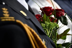 Zdjęcie kolorowe. Widoczny fragment munduru oraz bukietu kwiatów