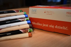 Zdjęcie kolorowe. Widoczne czekolady oraz kartonik z napisem Słodko jest się dzielić