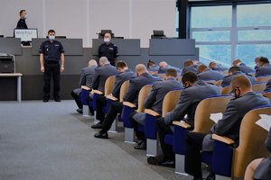 Zdjęcie kolorowe. Widoczna aula komendy wojewódzkiej policji oraz umundurowani policjanci podczas egzaminu oficerskiego