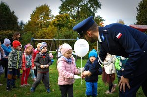 Policjant wręcza dziewczynce balonik, w tle grupa dzieci