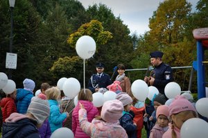 Policjanci z grupą przedszkolaków, które trzymają balony na placu zabaw