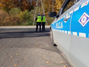 Policjanci podczas kontroli prędkośći na drodze. Z prawej fragment radiowozu.