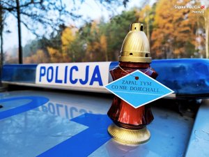 Fragment radiowozu z napisem policja, a na nim znicz z zawieszką o treści zapal tym, co nie dojechali.