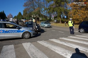 Policjanci kierują ruchem na drodze przy przejściu dla pieszych i w okolicy cmentarza.