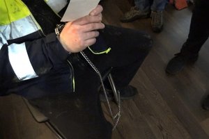 Na zdjęciu zatrzymany mężczyzna z kajdankami zespolonymi. Trzyma w dłoniach dokument dotyczący podstawy zatrzymania.