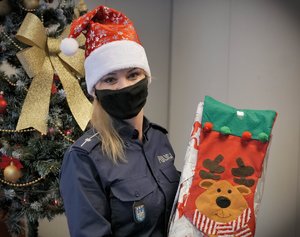 Umundurowana policjantka w czapce świętego Mikołaja trzyma prezent.