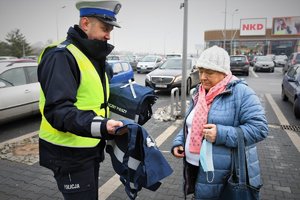 policjant ruchu drogowego wręcza seniorce torbę na zakupy z elementami odblaskowymi i napisem &quot;Bezpieczny pieszy&quot;