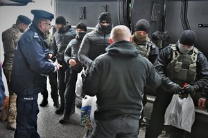 Zdjęcie kolorowe. Widoczni umunudrowani policjanci, w tym Zastepca Komendanta Wojewódzkiegoi, w tle policyjny samochód