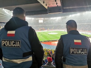 Zdjęcie kolorowe. Widoczny policjant na terenie stadionu