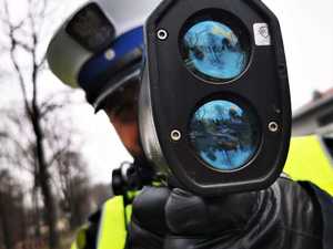 Na fotografii widać policjanta wydziału ruchu drogowego, który mierzy prędkość pojazdu za pomocą laserowego miernika prędkości.