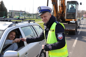 Na zdjęciu widać policjanta wydziału ruchu drogowego, który wręcza kierującemu naklejkę w kształcie koła z napisem: Prowadzę jestem trzeźwy