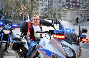 Dziecko siedzi na policyjnym motocyklu, trzyma flagę Polski.