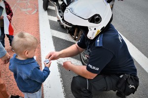 Policjant w kasku wręcza dziecku odblaskową opaskę.