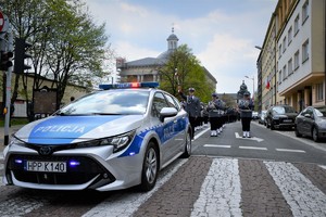 Policyjna orkiestra podczas przemarszu na Plac Sejmu Śląskiego., przed nią stoi oznakowany radiowóz.