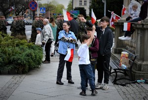 Dzieci obserwują defiladę, mają w rękach flagi Polski.