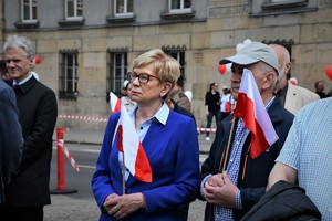 Uczestnicy uroczystości. Kobieta i mężczyzna trzymają flagi Polski.