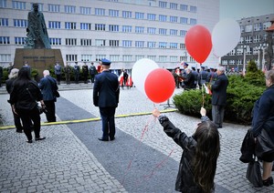 Widoczna sylwetka dziewczynki z tyłu, która trzyma w dłoniach białe i czerwone baloniki. W dalszej części pomnik Wojciecha Korfantego i uczestnicy uroczystości.