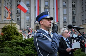 Policjant w galowym umundurowaniu, który był dowódcą uroczystości. W tle flagi Polski.
