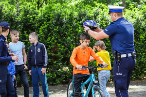 Policjant zakłada siedzącemu na rowerze dziecku kask.