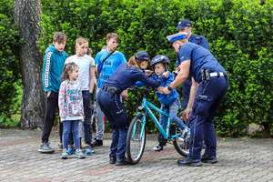 Policjantka zapina kask dziecku, które siedzi na rowerze. Obok stoi policjant.