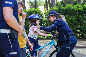 Policjantka zapina siedzącej na rowerze dziewczynce kask.