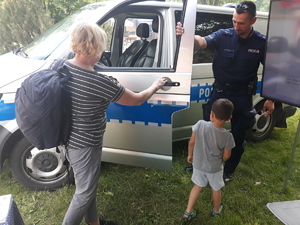 Policjant otwiera drzwi radiowozu i pokazuje wnętrze dziecku i kobiecie