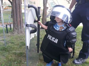 Chłopiec ubrany w kamizelkę, kask, z tarczą policyjną